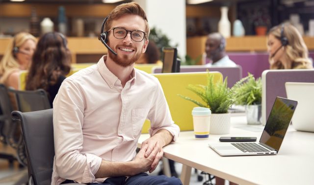 Portrait Of Businessman Wearing Headset Talking To Caller In Customer Services Centre